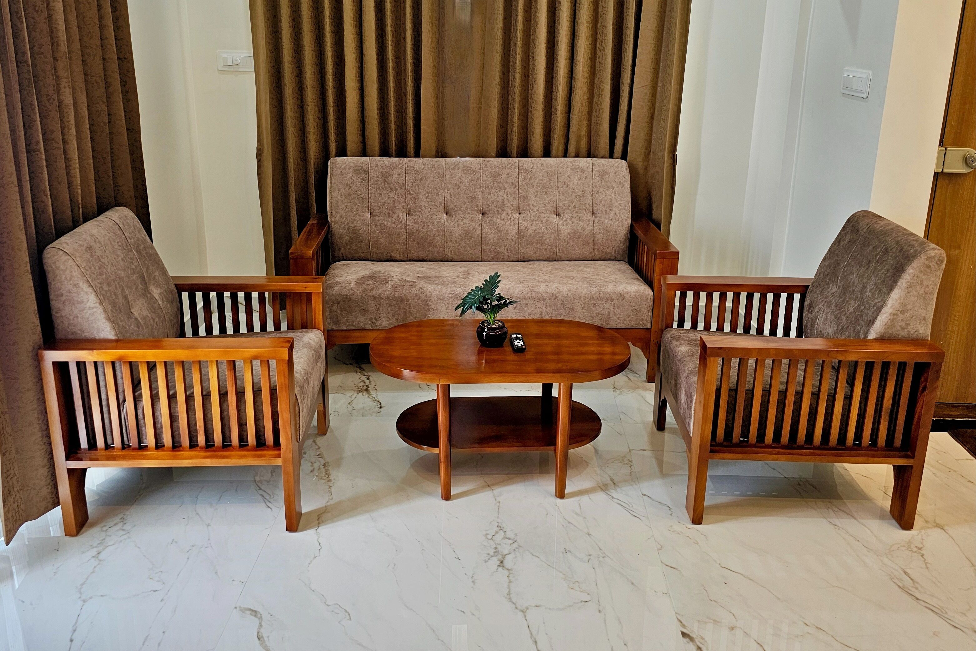 Uma sala de estar com um sofá bege, duas poltronas de madeira e uma mesa de centro redonda de madeira.