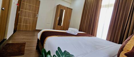 A hotel room with a bed, a wardrobe, a mirror, and a window with curtains.