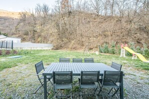Une table de pique-nique avec des chaises, une aire de jeux avec un toboggan et une colline en arrière-plan.