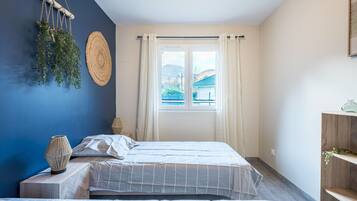 A bedroom with two beds, a window with curtains, a wall-mounted plant, and a woven lamp.