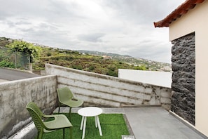 Una terraza con dos sillas verdes, una mesita blanca y vistas a un paisaje montañoso.