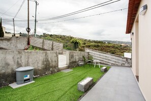 A rooftop terrace with artificial grass, a concrete planter, and a trash bin.