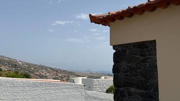 A balcony with a view of a coastal town, a stone wall, and a green chair.