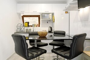 A modern kitchen with a glass table, four black chairs, a microwave, and a refrigerator.