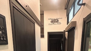 Un pasillo con alfombra a cuadros, una puerta con cerradura electrónica y un cartel en la pared que dice 'Life's an Adventure Enjoy the Ride'.