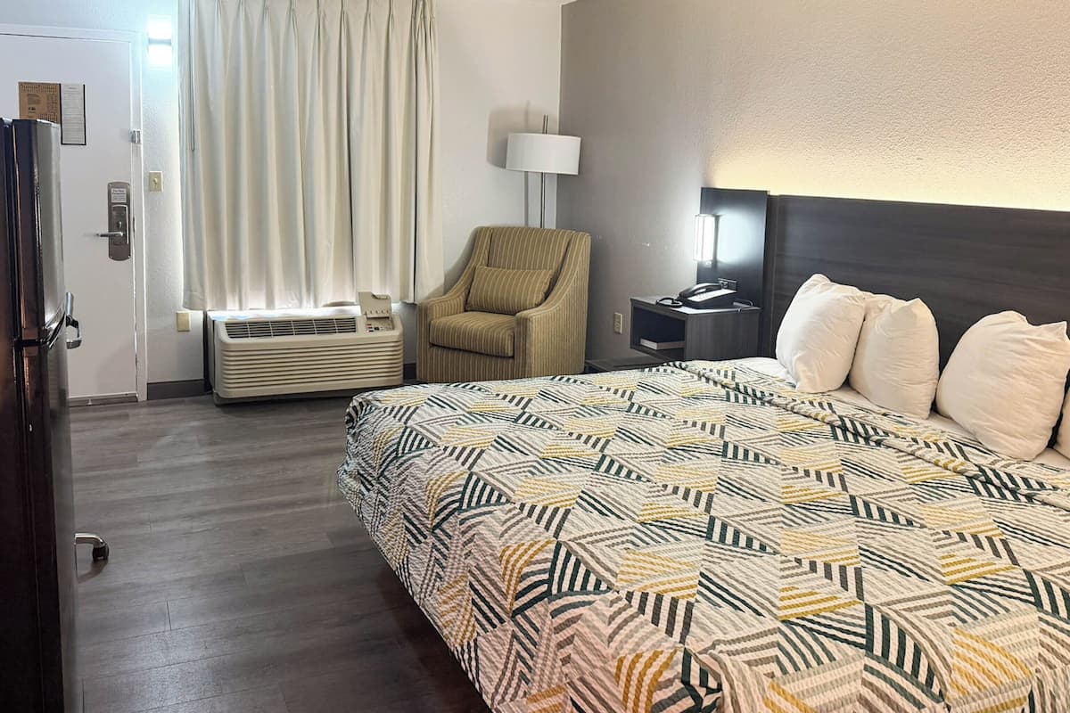 A hotel room with a bed, a chair, a bedside table, a lamp, and a wall-mounted phone.