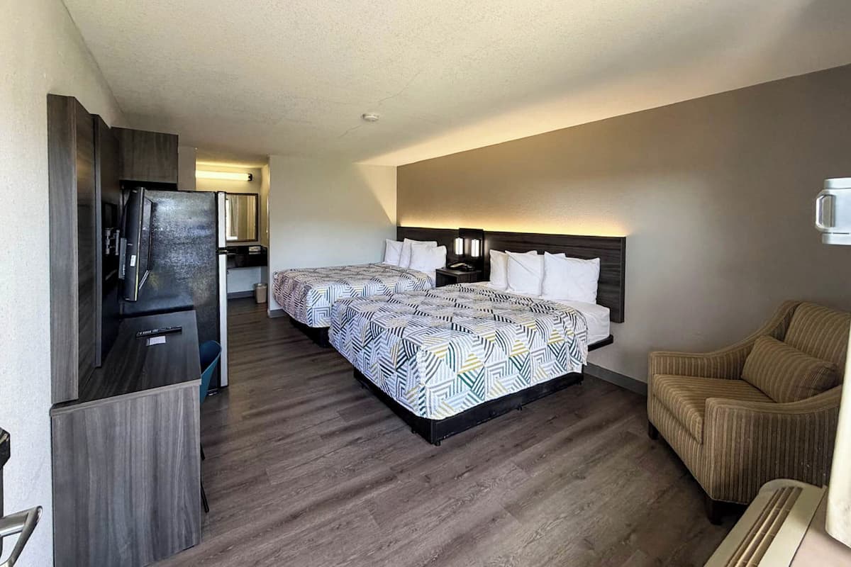 A hotel room with two beds, a TV, a refrigerator, a chair, and a small kitchenette.