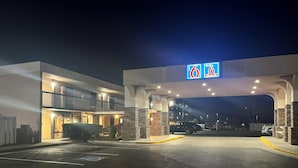 A 6th Street hotel entrance at night with a modern design, featuring a large sign above the entrance and a parking lot in front. - Studio 6 - Stafford, Va - Quantico (Stafford)