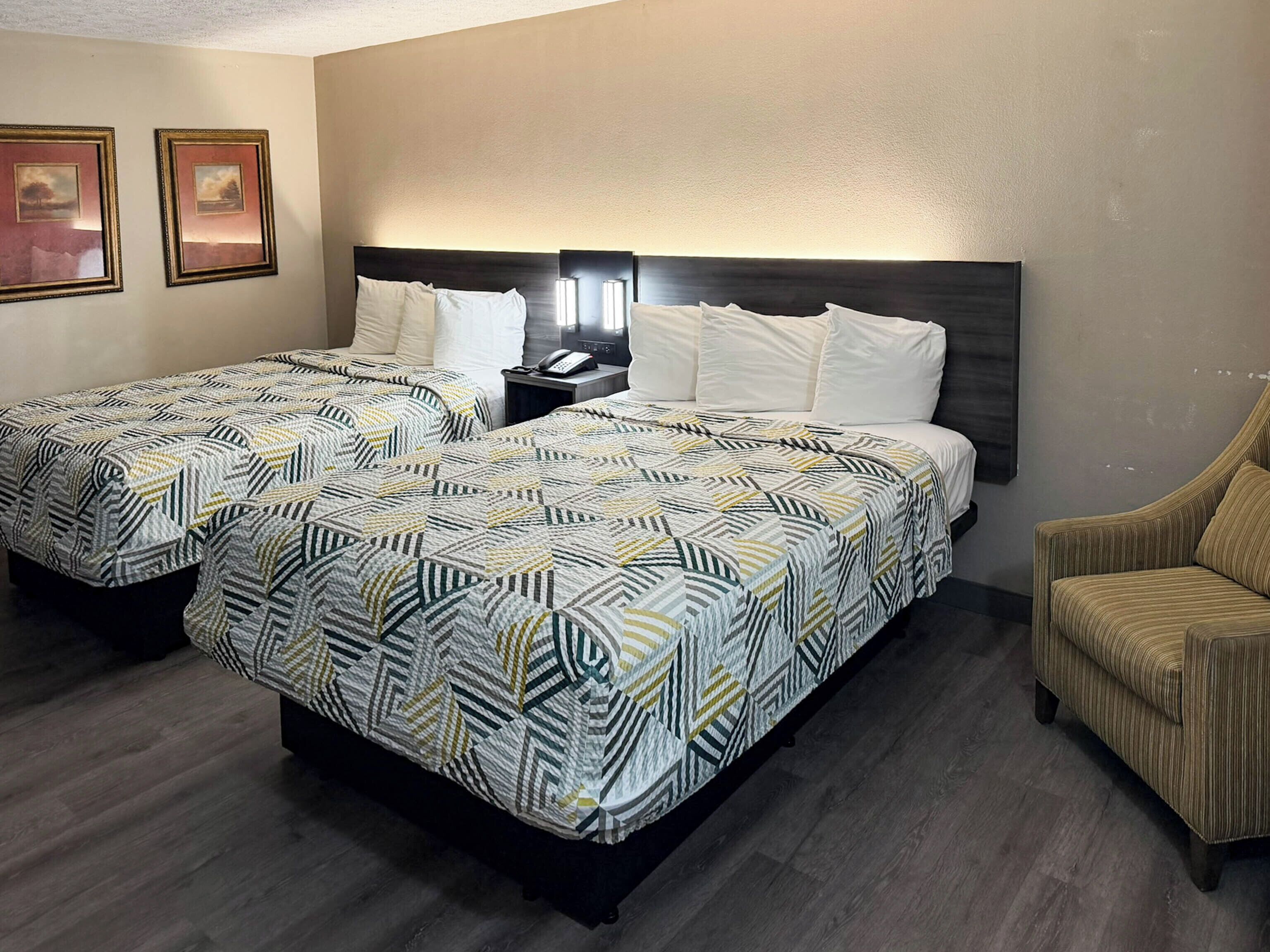 Habitación de hotel con dos camas, una mesita de noche, una silla y cuadros en la pared.