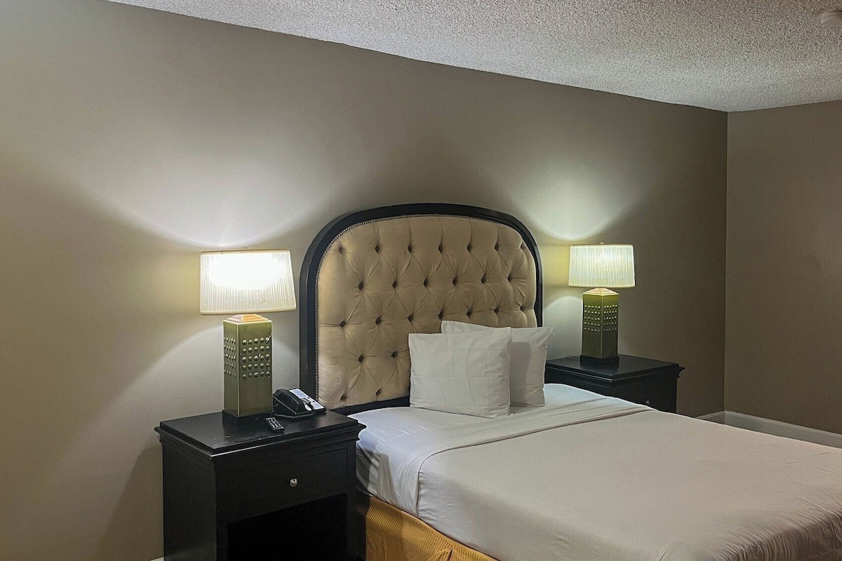 A hotel room with a large bed, two bedside tables with lamps, a headboard, and a nightstand.