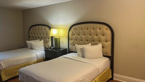 A hotel room with two beds, each with a tufted headboard and white bedding. A nightstand with a lamp and a telephone is between the beds. - MOTEL 6 Victorville Green Tree Blvd (Victorville)