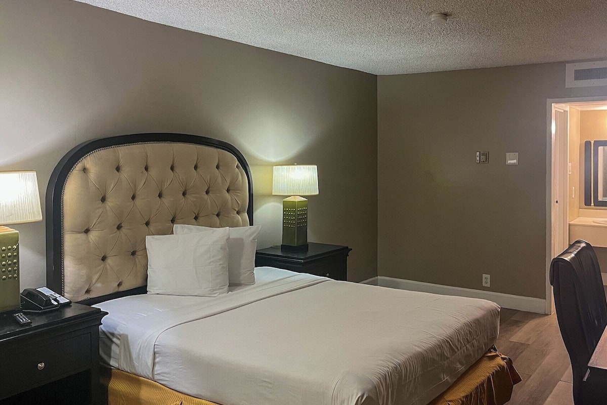 A hotel room with a large bed, two bedside tables with lamps, a desk, and a chair.