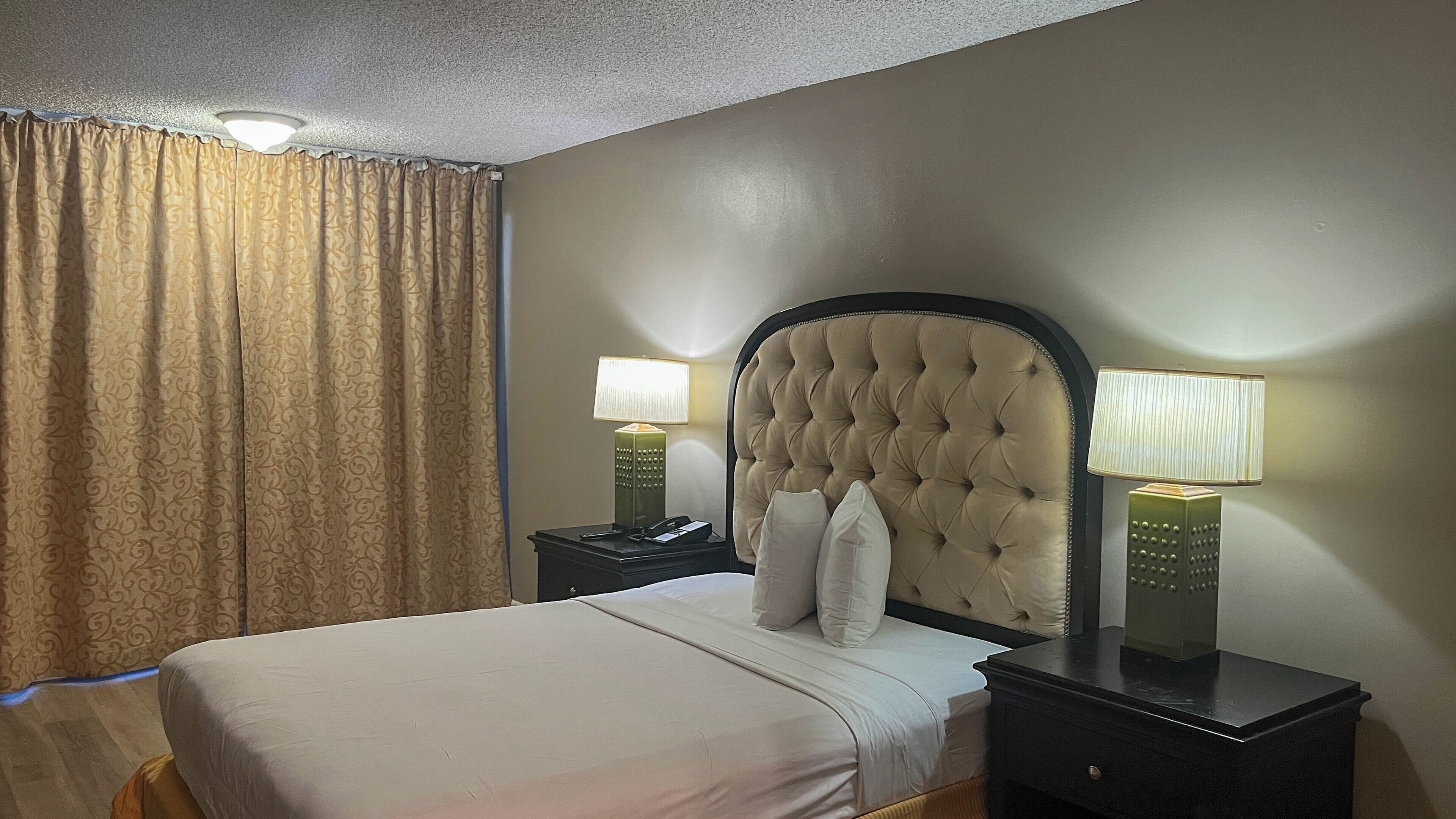 A hotel room with a large bed, two bedside tables with lamps, a headboard, and a curtain.