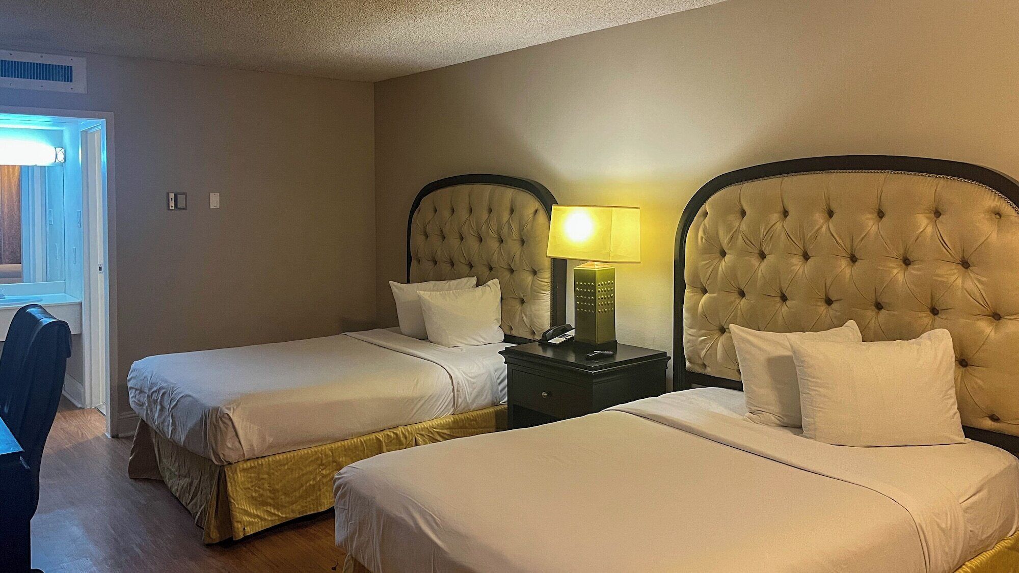 A hotel room with two beds, a nightstand with a lamp, and a window with blinds.