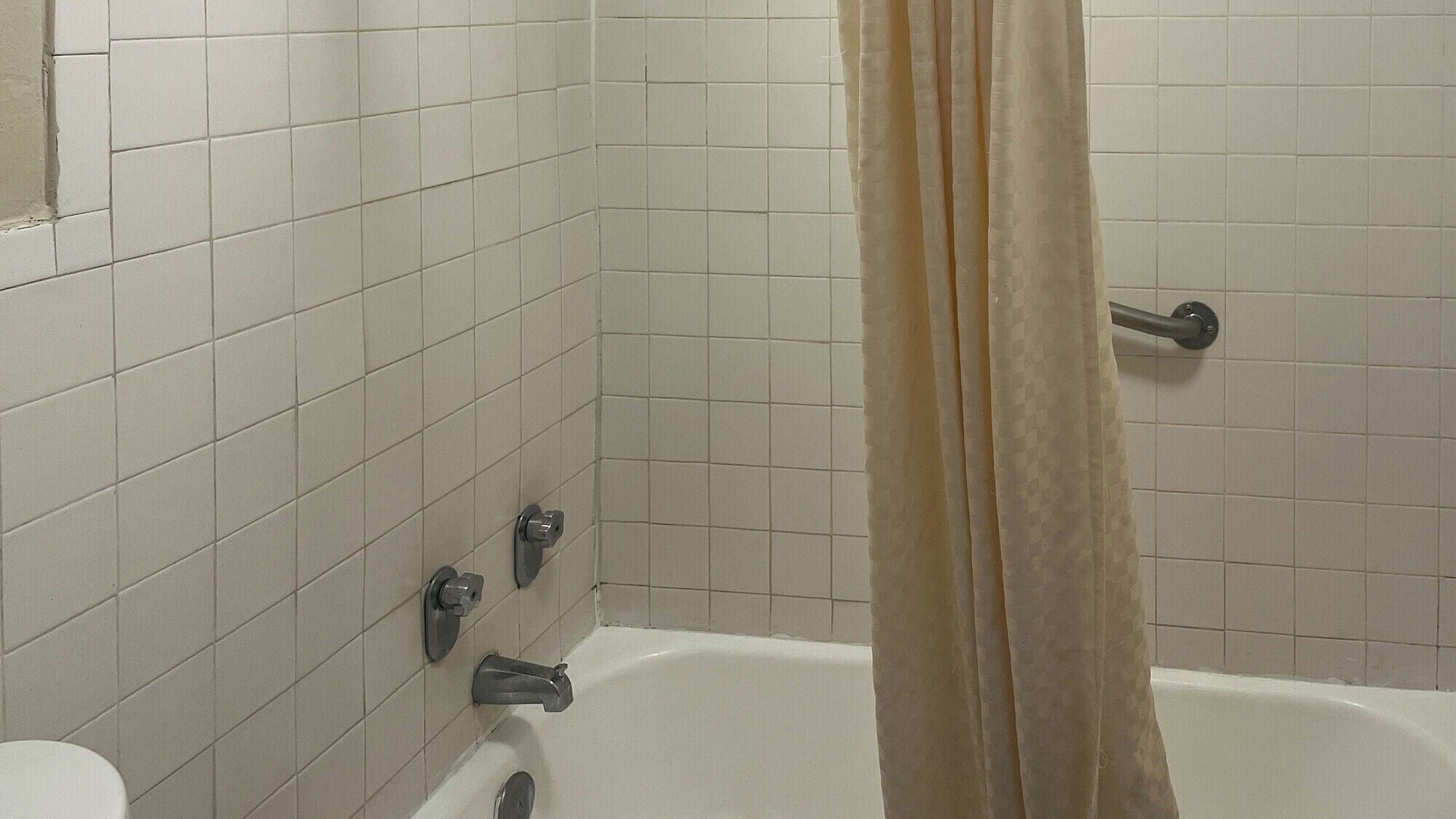 Une salle de bain avec des murs recouverts de carreaux blancs, une baignoire et un rideau de douche.