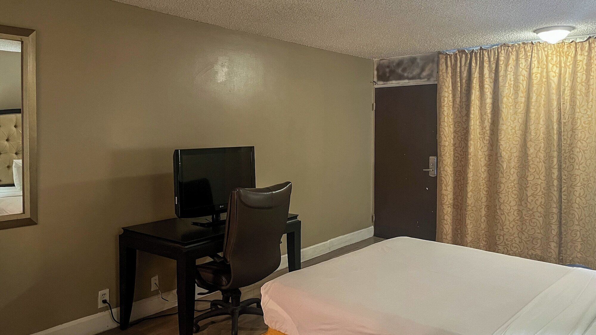 A hotel room with a bed, a desk with a television, and a door.