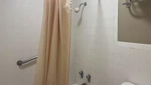 A bathroom with white tiled walls, a shower curtain, a grab bar, a toilet, and a mirror. - MOTEL 6 Victorville Green Tree Blvd (Victorville)