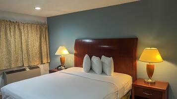 A hotel room with a large bed, two bedside lamps, a wooden headboard, and a window with curtains.
