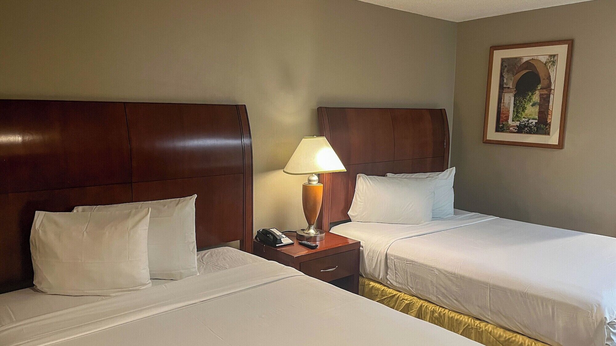 A hotel room with two beds, a nightstand with a lamp, a phone, and a painting on the wall.