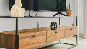 Ett modernt vardagsrum med en stor platt-TV som är monterad på väggen, ett träbord med lådor, en krukväxt och en dekorativ skulptur.