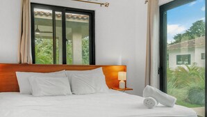 Ett hotellrum med en säng, ett nattduksbord med en lampa och utsikt över grönskan genom fönstret.