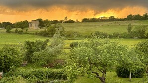 Een historisch stenen gebouw in een weelderig groen veld, met een spectaculaire zonsondergang op de achtergrond.