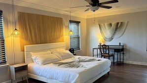 Un dormitorio ordenado con cama, mesitas de noche, un escritorio y un ventilador de techo.