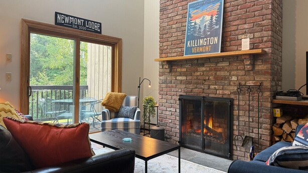 A cozy living room with a fireplace, a sign reading "NEWMONT LODGE Est. 2020", and a poster of "KILLINGTON VERMONT". - NewMont Lodge- Pool, Tennis court, pool table (Killington)