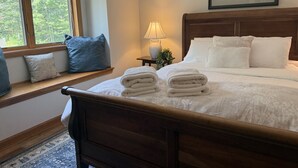 A neatly made bed with white linens and towels, a bedside lamp, and a framed picture on the wall. - NewMont Lodge- Pool, Tennis court, pool table (Killington)