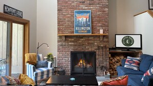A cozy living room with a brick fireplace, a blue sofa, a striped armchair, and a coffee table. - NewMont Lodge- Pool, Tennis court, pool table (Killington)