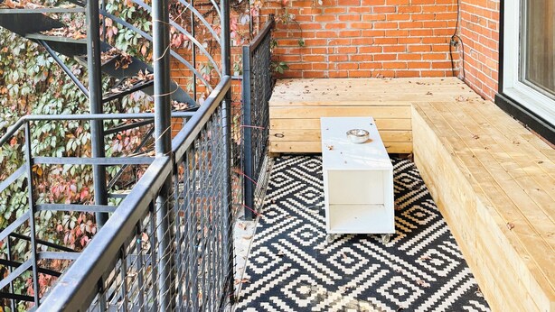 A cozy outdoor seating area with a patterned rug, a wooden bench, and a metal staircase.
