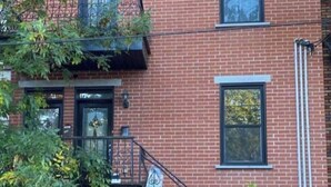 A two-story brick building with a black metal fire escape, a black door, and a small window.