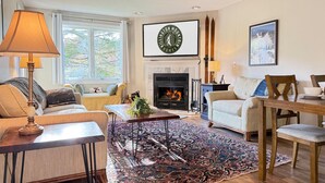 A cozy living room with a fireplace, a large rug, and a television mounted above it.