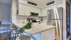 A modern kitchen with white cabinets, a stainless steel refrigerator, and a bar area with stools.