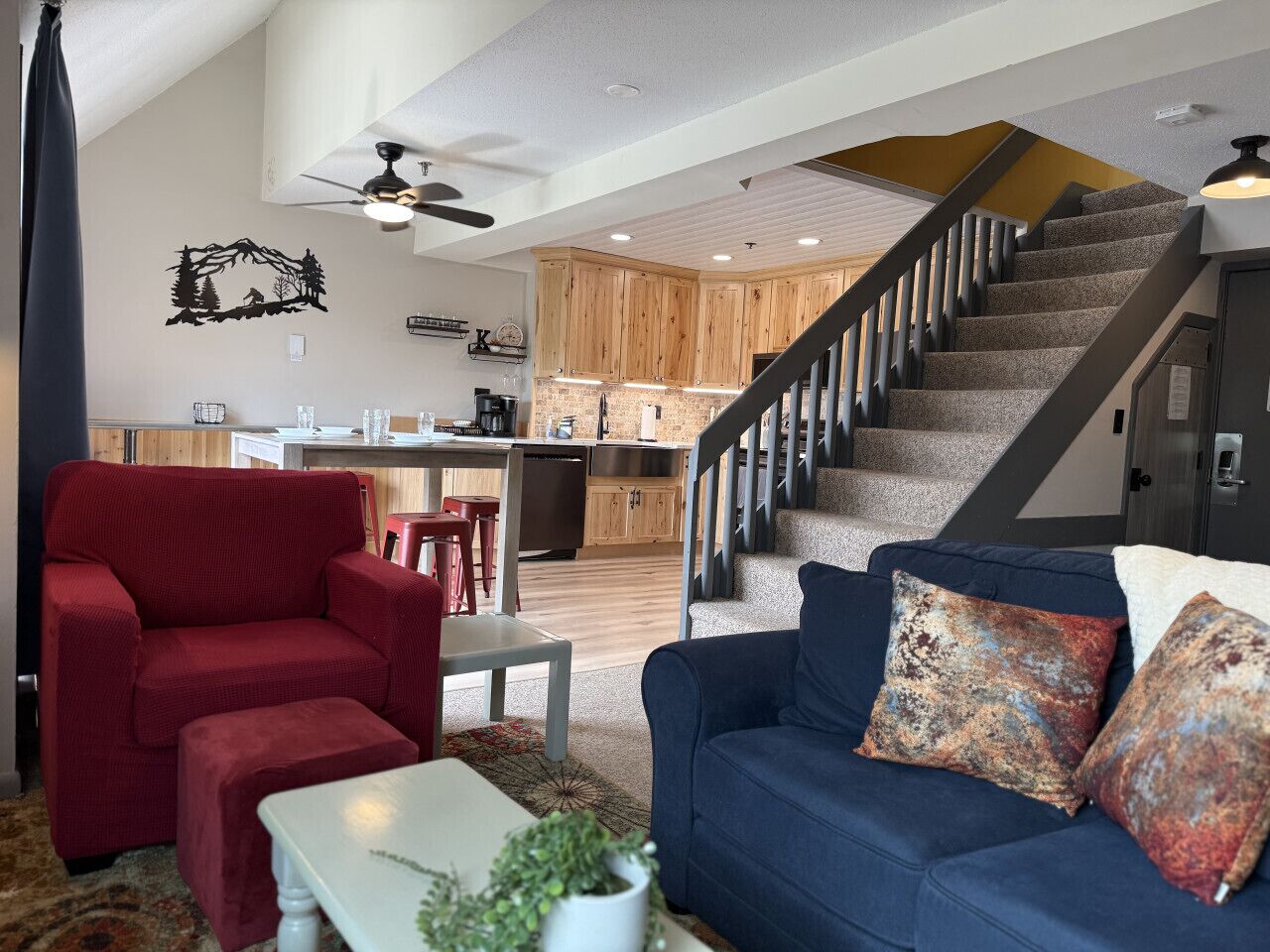 A spacious living area with a red armchair, a blue sofa with patterned cushions, a white coffee table, and a staircase leading to an upper level.