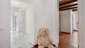 Un oso de peluche grande en un pasillo con piso estampado y vigas de madera.