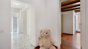 Un pasillo con un osito de peluche grande, paredes blancas y suelo de madera.