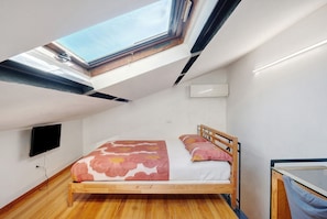A bedroom with a skylight, a bed, a TV, and a wooden floor.