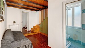 Una habitación con techo de madera, un sofá, una escalera y un baño con inodoro y toallero.