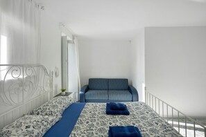 Un dormitorio con una cama, un sofá, una barandilla blanca y una puerta que da a otra habitación.