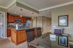 A modern kitchen with wooden cabinets, a glass island, and a dining area with a glass table and chairs.