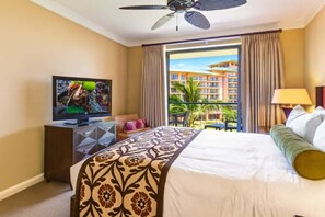 Une chambre d’hôtel équipée d’un lit, d’une télévision, d’un ventilateur de plafond, d’une fenêtre avec des rideaux et offrant une vue sur un immeuble.