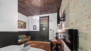 A hotel room with a bed, a sofa, a television, a wooden table with a lamp, a patterned rug, and a decorative ceiling. - Swedetown European Style Hostel (Duluth)