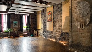 A spacious room with exposed brick walls, a wooden floor, and a large dreamcatcher hanging on the wall. - Swedetown European Style Hostel (Duluth)