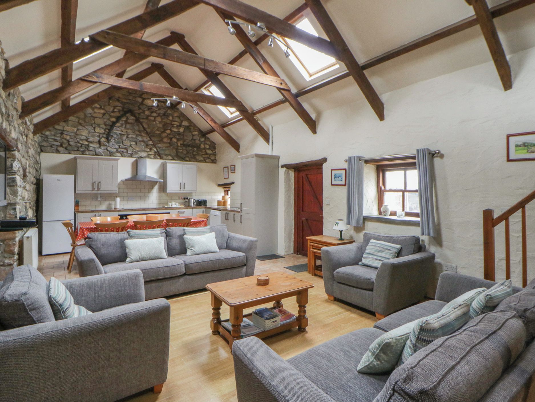 A spacious living area with a stone wall, wooden beams, and a kitchen in the background.