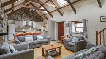 A spacious living area with a stone wall, wooden beams, and a kitchen in the background.