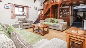 Una sala de estar acogedora con un techo alto de madera, una escalera que sube a un nivel superior y una chimenea.