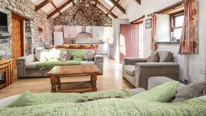 Una sala de estar acogedora con pared de piedra, vigas de madera y vistas a la cocina.