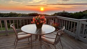 A deck with a round table and chairs, a vase of flowers, and a sunset view. - Amazing sunsets, a welcoming home, and island adventures.  Lifetime memories! (Chilmark)