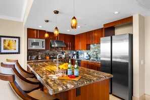 Une cuisine dotée de meubles en bois, d’un réfrigérateur en acier inoxydable, d’un plan de travail en granit et de luminaires suspendus.